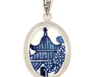 May include: Oval pendant with a silver-tone frame. The pendant features a blue and white design of a pagoda and foliage. The bail is also silver-toned with an ornate design. The pendant is a classic piece of jewelry.