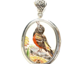 May include: A silver oval pendant with a porcelain inset featuring a painted image of a brown and orange bird with yellow accents, perched on a rock with yellow flowers.