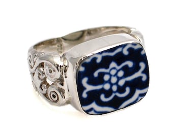 May include: A silver ring with a blue and white ceramic inlay. The inlay features a floral design. The ring band is intricately detailed with a scroll design.