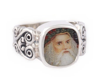 May include: A silver ring with a square-shaped bezel featuring a vintage portrait of a man with a beard and crown. The ring band has a decorative scroll design.