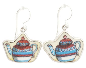 May include: A pair of silver dangle earrings with a teapot design. The teapot is white with blue and red stripes and a red lid.