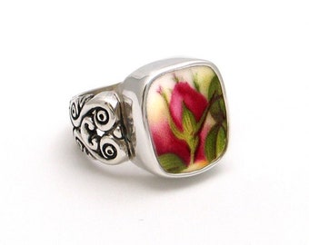 May include: A silver ring with a square shaped setting featuring a vintage floral design with a pink rose and green leaves.