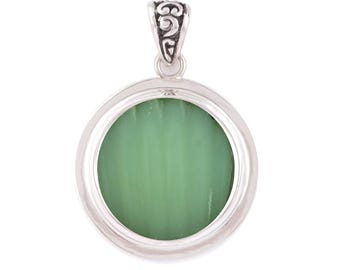 May include: A circular pendant featuring a smooth, light green stone set within a polished silver frame. The pendant includes a decorative silver bail at the top with intricate, swirling engraved patterns, providing a secure attachment point.