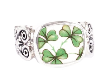 May include: A silver ring featuring a white and green shamrock design. The ring has an intricate band with a Celtic knot design.