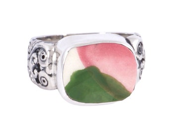 May include: A silver ring with a green, white, and pink stone set in a rectangular bezel. The band of the ring is decorated with a floral design.