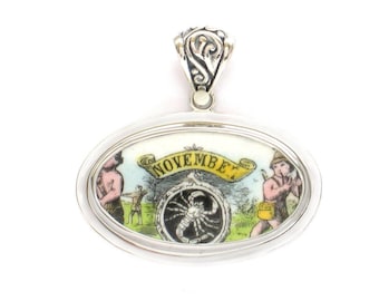 May include: Silver oval pendant with a colorful enamel image of a scorpion, the zodiac sign for November. The image also includes two figures, one holding a bow and arrow and the other playing a flute.