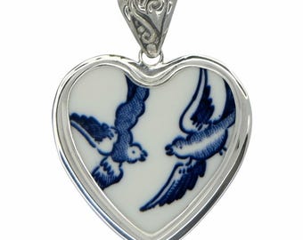 May include: Heart-shaped pendant with a silver-tone frame and bail. The pendant features a white ceramic insert with a blue and white bird design. The birds are depicted in flight, facing each other.
