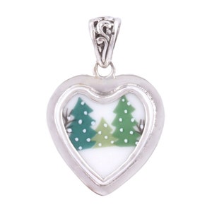May include: A silver heart-shaped pendant with a white background and a green and white image of two pine trees inside. The pendant has a silver bail.