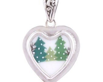 May include: A silver heart-shaped pendant with a white background and a green and white image of two pine trees inside. The pendant has a silver bail.