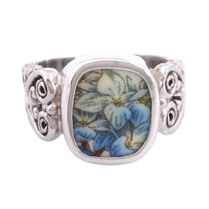 May include: A silver ring with a square blue and white floral design. The ring has a decorative band with a swirl design.