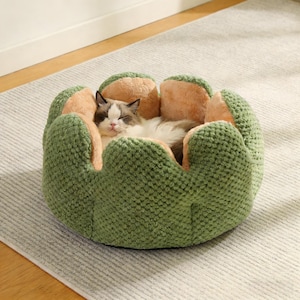 May include: A cat sleeps peacefully in a green and beige pet bed. The bed is designed to resemble a flower, with a textured, plush outer layer. The cat's fur is a mix of white, brown, and black.