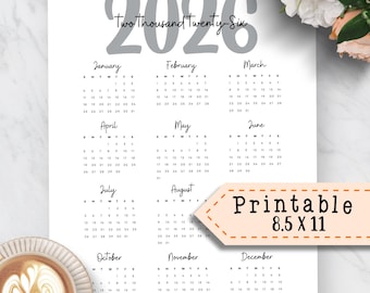May include: A white 2026 calendar with the text "Two Thousand Twenty-Six" in gray. The calendar includes the months January through December, with the text "Printable 8.5 X 11" in a brown banner. A cup of coffee is in the lower left corner.