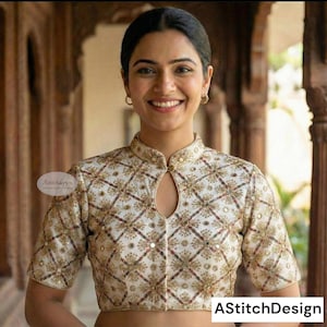 Puede incluir: Blusa color crema de manga corta con cuello alto y bordados dorados intrincados en un patrón geométrico. La blusa tiene un detalle de ojo de cerradura en el escote y está adornada con pequeños acentos redondos y reflectantes. El texto "AStitchDesign" es visible.