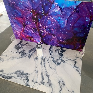 Puede incluir: Un telón de fondo de mármol blanco y negro con una pequeña botella transparente con tapa negra en el centro.