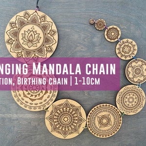 May include: A hanging wooden mandala chain with 10 circular wooden pieces, each with a different intricate mandala design. The chain is made of string and the mandalas range in size from 1 to 10 centimeters in diameter.  The mandalas are all brown and black and have a natural wood finish.  The chain is hanging against a gray wooden background.  The text "HANGING MANDALA CHAIN DILATION, BIRTHING CHAIN | 1-10CM" is printed in white on a pink background.