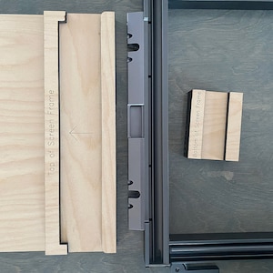 May include: Four pieces of wood with text on them. The pieces are labeled "Left Side of Glowforge", "Top of Screen Frame", "Bottom of Screen Frame", and an arrow pointing to the right. The pieces are on a gray surface.