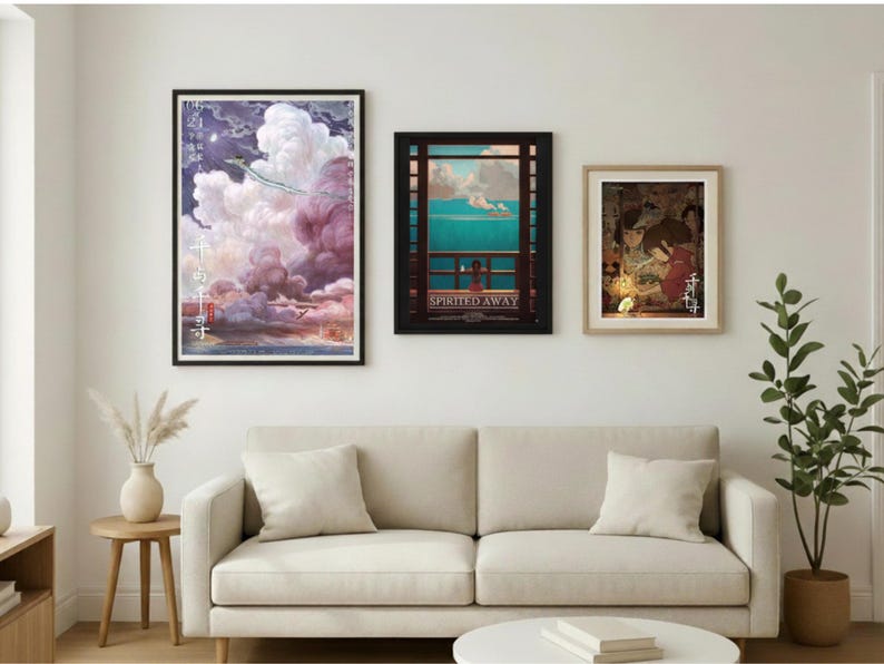 May include: Three framed art prints hang above a cream-colored sofa. The prints feature colorful illustrations, including a scene with a dragon and clouds, a coastal view, and a traditional Japanese scene. The room is decorated with a vase of dried flowers and a potted plant.