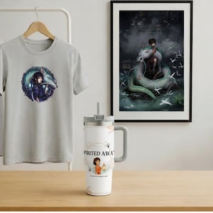 May include: A light gray t-shirt with a circular graphic featuring a character and a dragon. A white tumbler with a handle and the words "Spirited Away" is on a wooden surface. A framed print of a dragon and a person is on the wall.