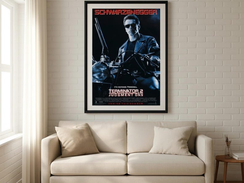Puede incluir: P&oacute;ster enmarcado de la pel&iacute;cula "Terminator 2: El Juicio Final" con Arnold Schwarzenegger. El p&oacute;ster tiene un marco negro y est&aacute; colgado sobre un sof&aacute; beige. El t&iacute;tulo y el nombre del actor son en rojo y blanco.