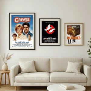 Puede incluir: Tres carteles de pel&iacute;culas enmarcados cuelgan sobre un sof&aacute; beige. Los carteles son de "Grease", "Ghostbusters" e "Incendies". El cartel de "Grease" muestra el t&iacute;tulo de la pel&iacute;cula y los actores. El cartel de "Ghostbusters" tiene el logotipo. El cartel de "Incendies" muestra un rostro femenino.