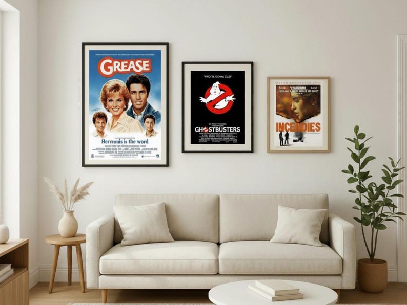 Puede incluir: Tres carteles de pel&iacute;culas enmarcados cuelgan sobre un sof&aacute; beige. Los carteles son de "Grease", "Ghostbusters" e "Incendies". El cartel de "Grease" muestra el t&iacute;tulo de la pel&iacute;cula y los actores. El cartel de "Ghostbusters" tiene el logotipo. El cartel de "Incendies" muestra un rostro femenino.
