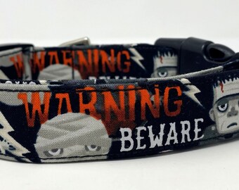 Puede incluir: Collar de perro negro y blanco con temática de Halloween. El collar presenta un patrón repetitivo de monstruo de Frankenstein, momias y el texto "WARNING BEWARE".