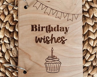 May include: A wooden book with a ring binding. The cover is light brown and has the text "Birthday wishes" with a cupcake illustration.