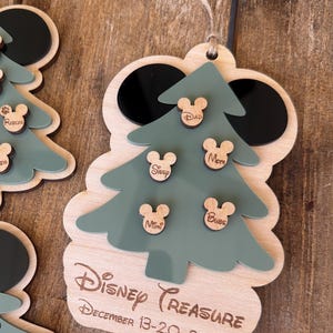 May include: Wooden Christmas ornament with a green tree design and Mickey Mouse head accents. The ornament has the words "Disney Treasure" and "December 13-20, 2025" engraved on it. Includes names like "Dad", "Mom", "Sissy", "Mimi", and "Bubs".