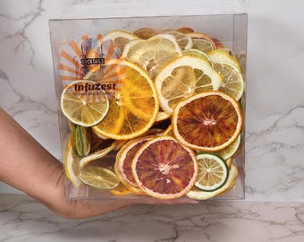 May include: A clear box containing dried citrus fruit slices, including oranges, lemons, and limes. The box has the text "Cocktails" and "Infuzest" printed on it. The fruit slices are various shades of yellow, orange, and red.