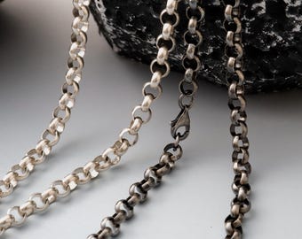 May include: Close-up of three silver-toned chain necklaces with a rounded link design. One chain has a clasp. The chains are displayed against a dark, textured background, highlighting the metallic shine of the jewelry.