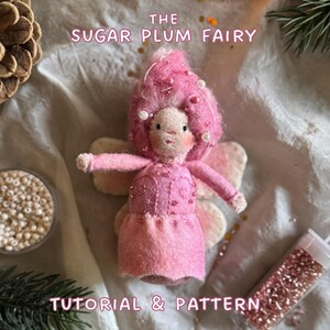 Könnte beinhalten: Eine handgefertigte rosa Feenpuppe mit einer flauschigen rosa Perücke und Perlenakzenten. Die Puppe trägt ein rosa Kleid und hat zarte Flügel. Der Text auf dem Bild lautet "THE SUGAR PLUM FAIRY TUTORIAL & PATTERN".
