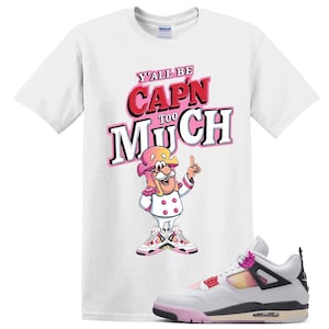 May include: A white short-sleeve t-shirt featuring a graphic of a cartoon character in a pink hat and white uniform with the text Y'ALL BE CAP'N TOO MUCH in pink and black lettering, paired with a white, pink, and black athletic sneaker.