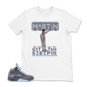 May include: White t-shirt with a graphic of a man pointing, the name "MARTIN" above him, and the phrase "GET TAH SLEEPPIN" below. A pair of gray and blue sneakers are in the foreground.
