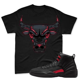 May include: Black t-shirt featuring a stylized bull head graphic in red and gray. Paired with black and red high-top sneakers. The bull graphic has intricate details, and the sneakers have red accents.
