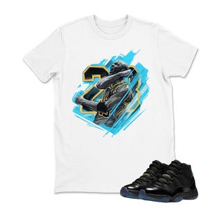 May include: White t-shirt featuring a graphic of a basketball player with the number 23, in black and gold, with a blue background. Black and blue sneakers are in the foreground.