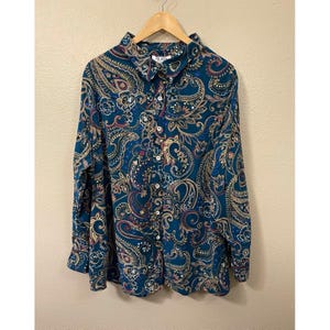May include: A long-sleeved button-down shirt in a deep teal color featuring a complex paisley pattern in shades of tan, cream, and dark red. The shirt has a standard collar, a full-length front button placket, and a label reading BLUES.
