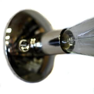 May include: A chrome-plated light fixture with a clear glass bulb. The fixture has a round base and a long, narrow neck.