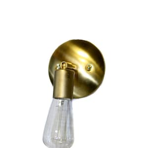 May include: A gold wall sconce with a round back plate and a single light bulb. The light bulb is a clear glass Edison bulb.
