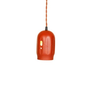 May include: A terracotta-colored pendant light with a ribbed texture and a small hole for light to shine through. The light is hanging from a long orange cord.