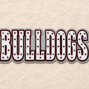 Puede incluir: Un parche decorativo con la palabra BULLDOGS en letras de bloque en negrita. Las letras son blancas con un borde granate y están cubiertas de pequeñas lentejuelas reflectantes con acentos granates dispersos por el diseño.