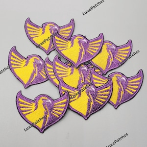 Könnte beinhalten: Eine Sammlung von gestickten Aufnähern, die einen stilisierten Adlerkopf mit ausgebreiteten Flügeln zeigen. Jeder Aufnäher hat ein leuchtend gelbes Adlerdesign auf einem tiefvioletten Hintergrund mit glitzernder Textur. Der Text LuxePatches ist sichtbar.