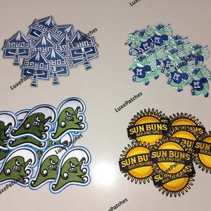 May include: A selection of embroidered patches with diverse designs. Includes patches with the text "FORGE", a stylized wave with a face, a logo with the text "SUN BUNS BAR AND GRILL", and a logo with the letter "M".
