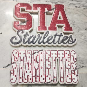 Puede incluir: Dos parches decorativos con la palabra Starlettes. El parche superior tiene letras de bloque rojas con lentejuelas que forman STA sobre la palabra Starlettes en cursiva oscura. El parche inferior muestra la palabra STARLETTES en blanco con detalles de lentejuelas rojas.