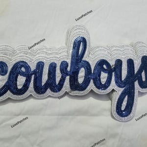 Op de afbeelding: Een pailletten patch met het woord "cowboys" in marineblauwe cursieve letters, omrand met zilveren pailletten. De patch heeft een zilveren glitterrand. Voor kleding.