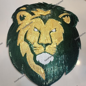 Op de afbeelding: Een grote, met pailletten bezette leeuwenkop-patch. De manen van de leeuw zijn donkergroen en het gezicht is goudkleurig. De ogen zijn wit en de neus is ook wit. De patch is waarschijnlijk voor kleding of accessoires.