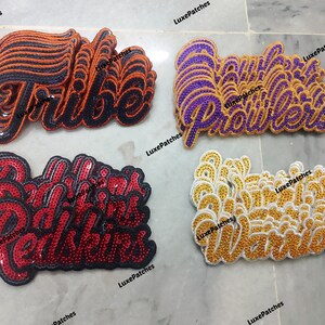 Könnte beinhalten: Vier Stapel bestickter Paillettenaufnäher mit den Wörtern Tribe in Orange und Schwarz, Prowlers in Lila und Gold, Redskins in Rot und Schwarz sowie Warriors in Gold und Weiß. Jeder Aufnäher hat eine Schreibschrift und eine geschichtete Textur.