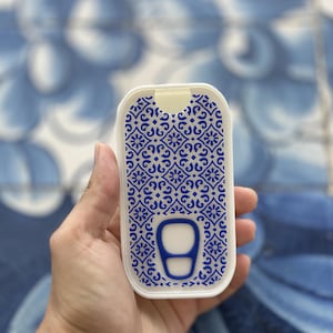 Op de afbeelding: Een rechthoekige witte plastic container met afgeronde hoeken, voorzien van een ingewikkeld blauw en wit bloemenpatroon op de voorzijde en een blauw accent in de vorm van een lipje onderaan het midden van het deksel.