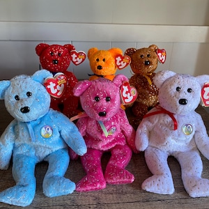 May include: A collection of six colorful plush teddy bears. The bears are in various colors, including red, orange, brown, blue, pink, and white. Each bear has a Ty heart-shaped tag attached to its ear.