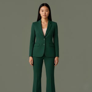 Könnte beinhalten: Ein dunkelgrüner Anzug bestehend aus einem Blazer und einer passenden Hose. Der Blazer hat einen Zwei-Knopf-Verschluss und Vordertaschen. Die Hose ist ausgestellt. Unter dem Blazer wird ein hellrosa Oberteil getragen.