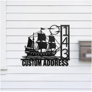 May include: A black metal wall sign featuring a silhouette of a sailing ship on waves with a full moon above. To the right, a vertical rectangular frame displays the numbers 1, 4, and 3 stacked. The text CUSTOM ADDRESS is centered below.
